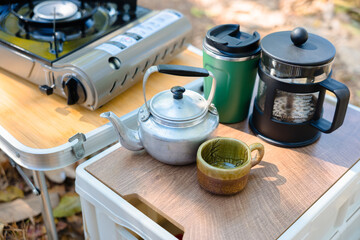 Outdoor camping coffee setup with kettle, ceramic mug, French press and portable gas stove on a table, showing simple travel lifestyle and cozy outdoor brewing