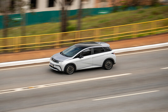 Silver BYD Dolphin electric car driving fast on highway panning shot
