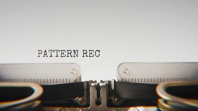 Old mechanical typewriter typing Pattern Recognition in a close-up view, with metal letters striking the white paper.