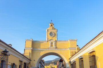 Historic Santa Catalina Arch with clock tower colonial architecture vibrant yellow facade blue sky heritage landmark street view iconic travel destination cultural charm in Antigua Guatemala