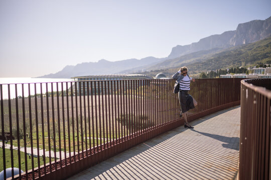 Woman balcony mountains, dramatic shadows stretching across modern architecture walkway. - Powered by Adobe