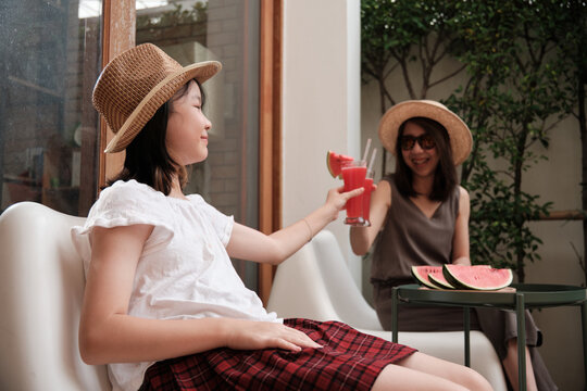 Chilling Asian family holidays, girl with casual hat and mum enjoy drinking fresh watermelon smoothies, happiness and cheerful relaxing on vacation with parent in hot summertime at outdoor terrace.