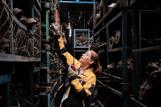 One Hispanic mature female inspector remotely works with walkie-talkie, checks auto spare parts stock in warehouse stack, operates jobs in manufacturing factory, and industrial worker occupation. - Powered by Adobe
