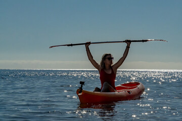 Woman, Kayak, Paddle. Young woman in kayak holding paddle overhead on sparkling blue sea during summer vacation with copy space