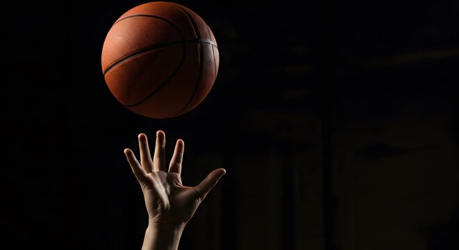 Basketball Player Hand Throwing Orange Ball in Dark Gym Lighting