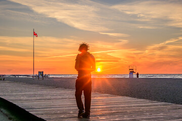 Silhouette of a person walking on a boardwalk along a beach at sunrise shot on Kew Beach in Toronto