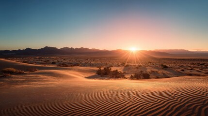 A stunning desert landscape at sunrise, featuring rippled sand dunes and distant mountains under a clear blue sky.