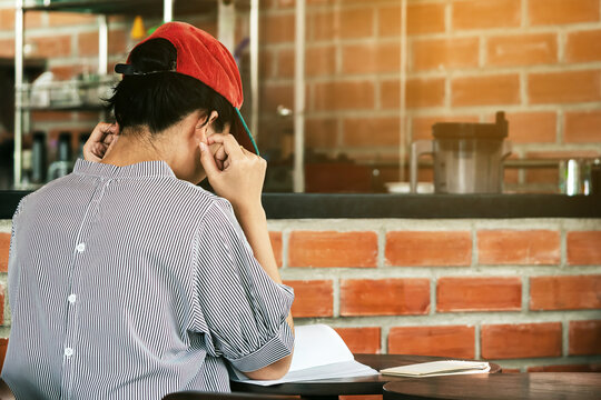 Young asian woman looking reading book and taking notes in cafe. Serious female student is sitting reading textbook preparing for exams. Female student stressed out and focused studying for exam.