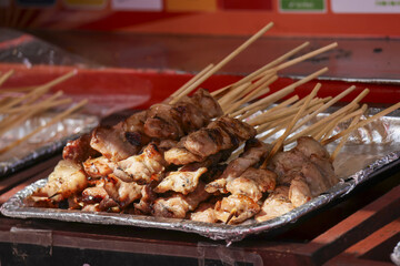 Delicious grilled chicken satay skewers on foil tray at an Asian street food market. Appetizing barbecue meat on stick, popular and savory traditional snack ready to eat