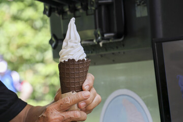 Person making delicious soft serve ice cream in chocolate cone from machine. This sweet, refreshing...