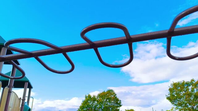 Kids playfully swinging on monkey bars under vibrant blue sky with fluffy clouds, enjoying outdoor fun and active lifestyle in the park on a sunny day creating happy childhood memories