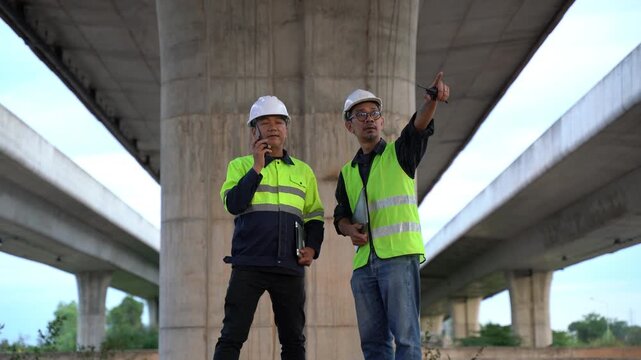 Construction workers discussing project details under a highway bridge, wearing safety gear, reflecting teamwork and collaboration in an urban environment