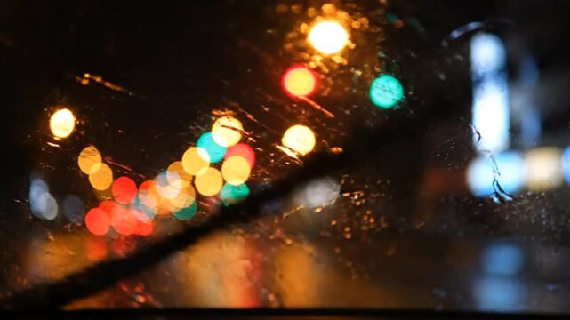 Raindrops on a car windshield with colorful out-of-focus city lights and bokeh at night during a rainy drive.