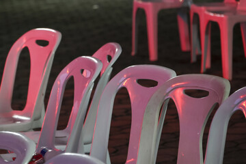 Rows of empty white plastic chair seating at an outdoor event at night. vacant chairs wait under...