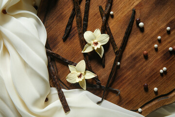Composition with vanilla sticks, flowers and light fabric on wooden background