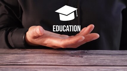 Close-up of a woman's hand on a table holding an animated graduation cap with the word "Education"