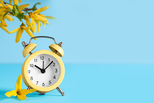 Alarm clock and blooming branch on blue background. Spring time - Powered by Adobe