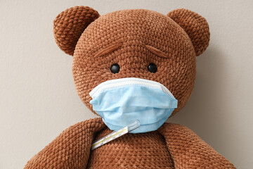Teddy bear in medical mask with thermometer on grey background