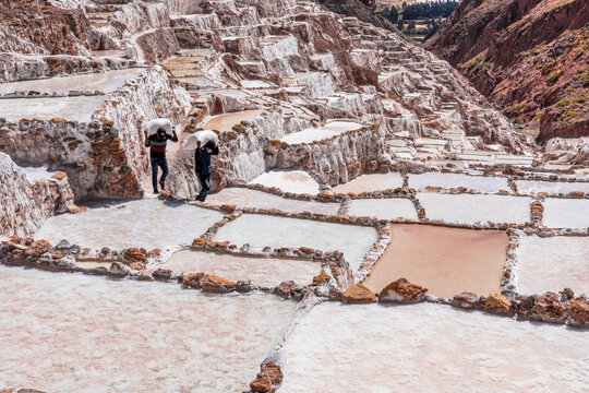 Two people working at the Maras Salt Mines, located in the district of Maras in the Sacred Valley of the Incas, Cusco.