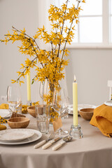 Elegant table setting with clean plates, burning candles, cutlery and blooming tree branches
