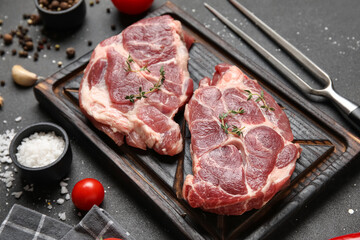 Wooden board with fresh raw steaks and different spices on black background, closeup