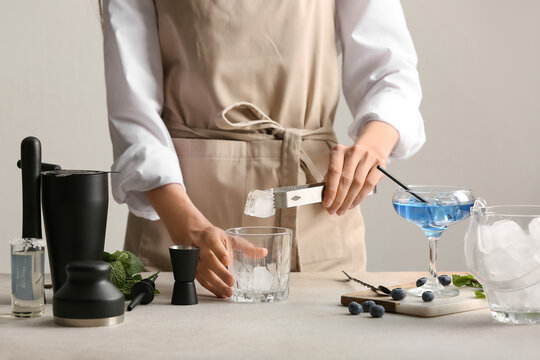 Female bartender making tasty cocktail  with blueberries and mint leaves at table against light background
