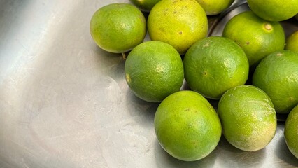 Fresh green limes gathered on a stainless-steel surface, with water droplets on both the limes and the surrounding area, giving a clean and refreshing appearance