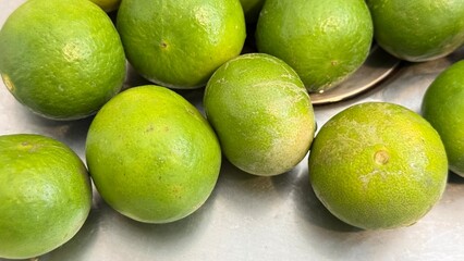 Fresh green limes gathered on a stainless-steel surface, with water droplets on both the limes and the surrounding area, giving a clean and refreshing appearance