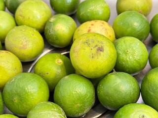 Fresh green limes gathered on a stainless-steel surface, with water droplets on both the limes and the surrounding area, giving a clean and refreshing appearance