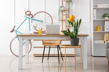 Interior of light home office with workplace, bicycle and plants
