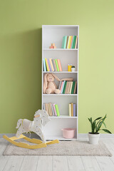 White bookshelf with toys near green wall in children's room