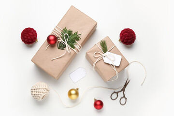 Gift boxes wrapped in eco paper with tags, Christmas decorations and packing materials on white background