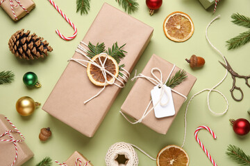 Gift boxes wrapped in eco paper with Christmas decorations, dried orange and packing materials on green background