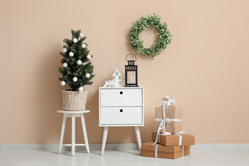 Interior of room with Christmas tree, gift boxes, wreath and lantern on bedside table near beige...
