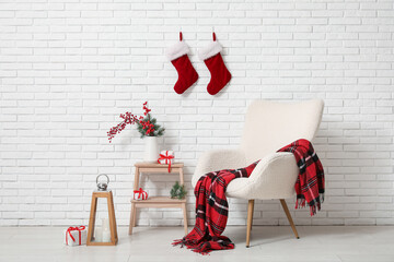 Obraz premium Interior of room with armchair, Christmas lantern, candles, gift boxes and red berries branches in vase on stepladder near white brick wall