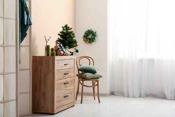 Fototapeta premium Interior of living room with folding screen, chair, Christmas tree, gift boxes and candles on commode near beige wall