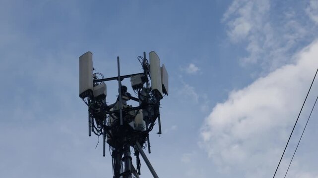 Cellular telecommunications tower with antennas and equipment against blue sky with white clouds and power lines