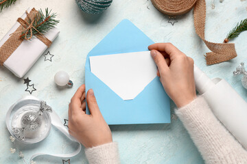 Female hands with blank greeting card in envelope, Christmas decorations and gift box on blue background