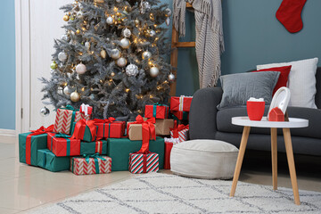 Interior of festive room with sofa, coffee table, Christmas tree and different many gift boxes near blue wall