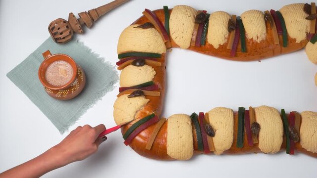 A person cutting a slice of king cake to celebrate Epiphany, Mexican rosca de reyes traditional bread.