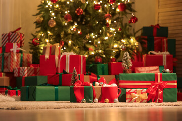 Many different gift boxes with decorations near Christmas tree in festive room at night
