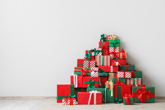 Heap of different many Christmas gift boxes near white wall in room