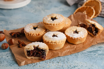 Board with tasty Christmas mince pies and dried oranges on grunge blue background