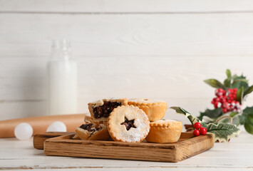 Board with tasty Christmas mince pies, bottle of milk and mistletoe branches on white wooden background