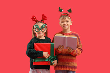 Naklejka premium Cute little children with book and Christmas gift on red background