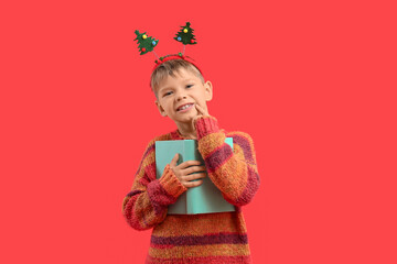 Naklejka premium Dreamy little boy with book on red background. Christmas celebration