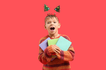 Naklejka premium Happy little boy with books on red background. Christmas celebration