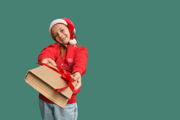 Naklejka premium Cute little girl in Santa hat with gift book on green background