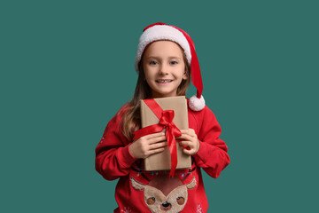 Naklejka premium Cute little girl in Santa hat with gift book on green background