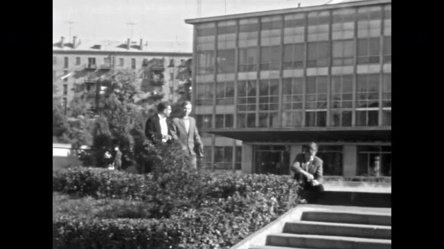 Positive businessmen discuss business and work on streets of summer city. Archival retro 1960s footage. Professionals walking and talking close modernist building. Old film. Vintage archive.